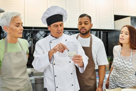 good looking mature chef discussing with his multiracial students how to bake, confectionary