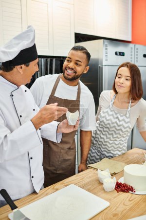cheerful african american man in apron next to his friend smiling at mature chef during lesson