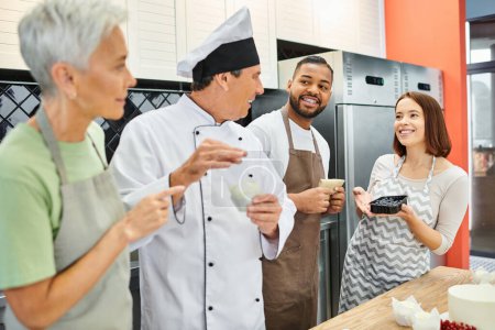 gente multicultural alegre en delantales hablando con cocinero maduro en sombrero blanco, cursos de cocina