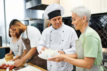 mature joyous chef in white hat teaching how to bake his interracial students during cooking lesson