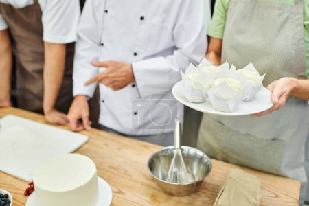 cropped view of mature chef showing how to bake to his multicultural students, cooking courses