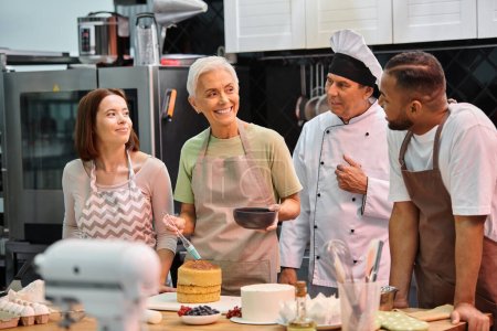 cheerful mature woman with silicone brush smiling at her diverse friends and chef in white hat
