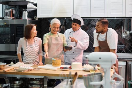 Photo for Chef explaining how to use silicone brush on cake to his mature student next to her diverse friends - Royalty Free Image