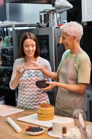 Téléchargez les photos : Jeune femme donnant brosse en silicone à son ami gai mature pour l'utiliser sur le gâteau, cours de cuisine - en image libre de droit
