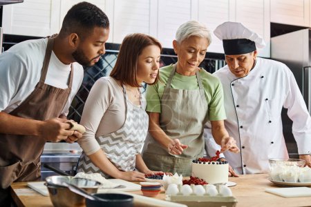 good looking diverse students looking at friend decorating cake next to mature chef in hat