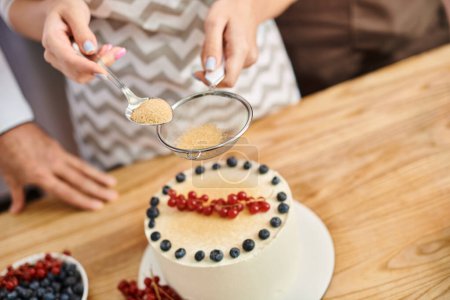 young woman with nail polish decorating delicious cake next to chef while on cooking lesson