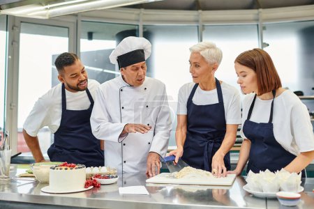Téléchargez les photos : Beau chef cuisinier mature en chapeau blanc expliquant comment faire cuire à ses chefs, confiserie - en image libre de droit