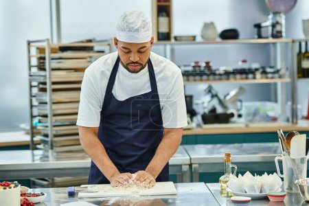 Téléchargez les photos : Beau chef afro-américain en tablier bleu travaillant avec de la pâte sur la cuisine, confiserie - en image libre de droit