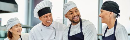 Téléchargez les photos : Jeune chef afro-américain avec toque et bretelles souriant à ses collègues à côté du chef cuisinier, bannière - en image libre de droit