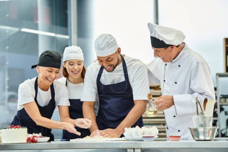 Téléchargez les photos : Joyeux beaux chefs travaillant avec de la pâte ensemble à côté de leur chef cuisinier, confiserie - en image libre de droit