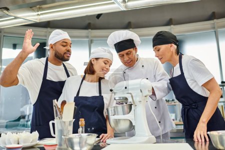 Téléchargez les photos : Chefs joyeux multiculturels regardant leur chef cuisinier leur montrant comment utiliser mélangeur, confiserie - en image libre de droit
