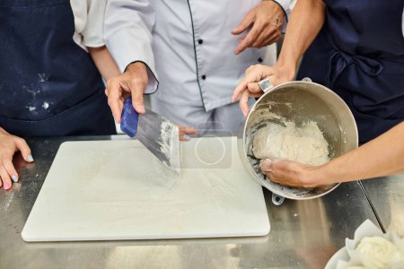 Téléchargez les photos : Vue recadrée du chef cuisinier mature montrant à ses cuisinières comment travailler avec de la pâte, confiserie - en image libre de droit