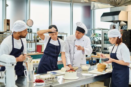 cocinero jefe maduro en sombrero blanco explicando cómo hornear a sus chefs multiculturales que trabajan duro