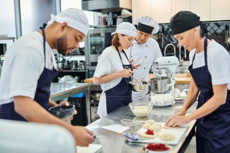 schöner reifer Chefkoch mit weißem Hut im Gespräch mit seinen hart arbeitenden multirassischen Köchen in der Küche