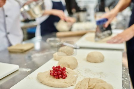 fokussierter Blick auf ungekochten Keks mit roter Johannisbeere auf dem Tisch neben Köchen und Chefköchen