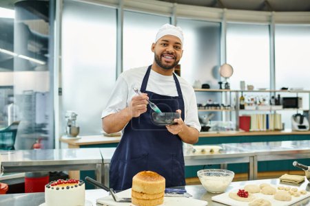 Foto de Atractivo cocinero afroamericano alegre en delantal usando cepillo de silicona y sonriendo a la cámara - Imagen libre de derechos