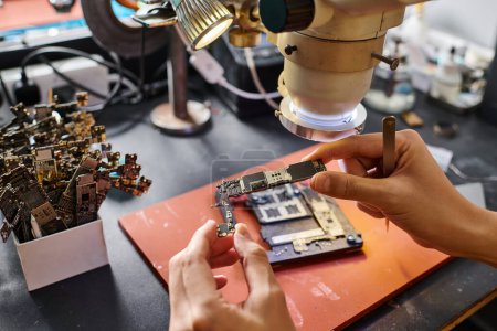 Ausgeschnittene Ansicht des Technikers, der den Chipsatz während der Reparatur des elektronischen Geräts in der Werkstatt hält