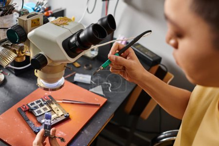 Asiatischer Reparateur testet Mikro-Schemata elektronischer Geräte in der Nähe professioneller Werkzeuge in der Werkstatt