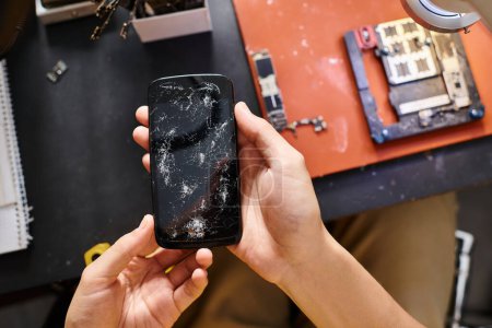 Handy mit kaputtem Bildschirm in den Händen eines qualifizierten Technikers in der Reparaturwerkstatt, kleines Unternehmen