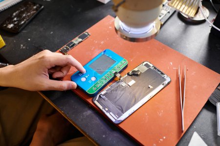 vista parcial del reparador haciendo diagnósticos de teléfono roto con voltímetro en taller privado