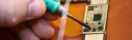 cropped view of skilled technician soldering electronic chipset in repair shop, horizontal banner