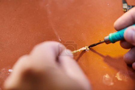 Teilansicht des gelernten Reparateurs beim Löten des Chipsatzes eines modernen elektronischen Gerätes in der Werkstatt
