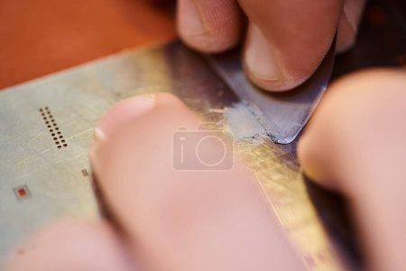 vista de cerca del técnico recortado rascando chipset electrónico en taller de reparación, pequeña empresa