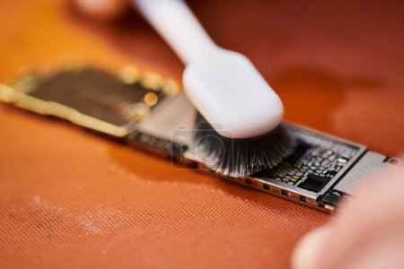 Ausgeschnittene Ansicht des Technikers Reinigung elektronischer Mikroschema mit Pinsel in professioneller Werkstatt