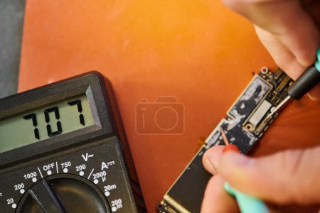 Ausgeschnittene Ansicht von professionellen Reparateuren, die Chipsätze mit Voltmeter in der Werkstatt testen, Kleinunternehmen