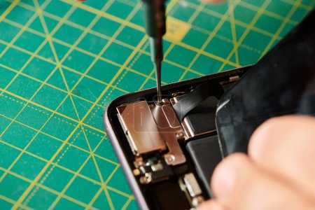 Téléchargez les photos : Vue recadrée du technicien ouvrant le téléphone portable avec tournevis pendant les essais dans son propre atelier - en image libre de droit
