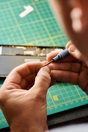 Téléchargez les photos : Vue recadrée d'un réparateur expérimenté tenant un tournevis près d'un téléphone portable dans un atelier privé - en image libre de droit