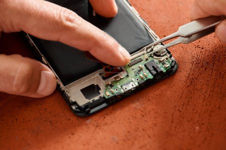 vista recortada de especialista técnico desconectando batería de smartphone con pinzas, mantenimiento