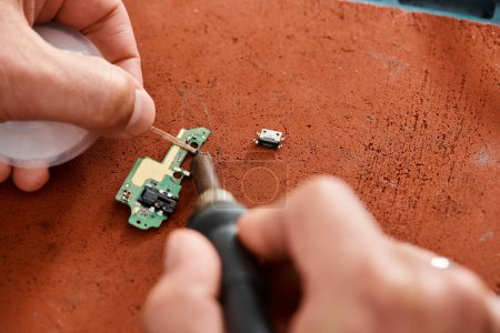 cropped view of skilled technician soldering electronic microscheme in workshop, small business