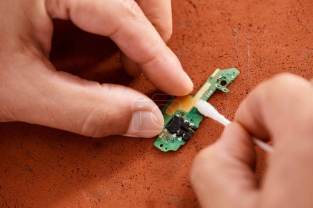 Téléchargez les photos : Vue recadrée du technicien nettoyage chipset électronique avec coton-tige, service d'entretien - en image libre de droit