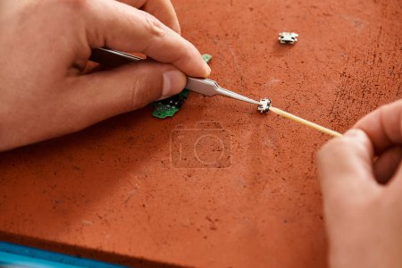 Ausgeschnittene Ansicht eines erfahrenen Reparateurs mit Pinzette beim Testen des elektronischen Chipsatzes in einer privaten Werkstatt