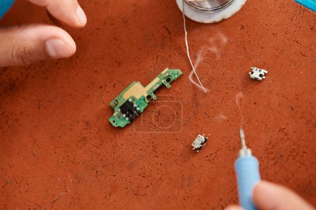Téléchargez les photos : Vue recadrée du réparateur professionnel avec fer à souder près de microschéma dans un atelier privé - en image libre de droit