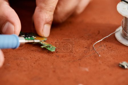 partial view of experienced technical specialist soldering electronic chip in repair workshop