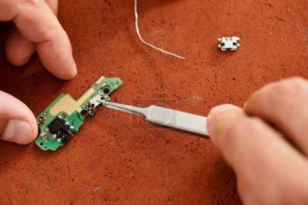 cropped view of professional technician with tweezers assembling electronic microscheme in workshop