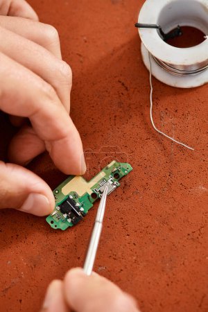 Ausgeschnittene Ansicht eines professionellen Reparateurs mit Pinzette, der den elektronischen Chipsatz in der Werkstatt testet