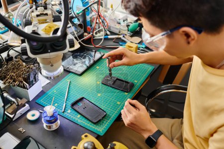 Foto de Reparador asiático con destornillador montaje de teléfono móvil trabajando en taller de reparación, pequeña empresa - Imagen libre de derechos