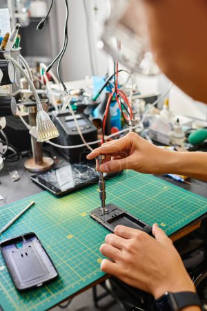 Ausgeschnittene Ansicht eines erfahrenen Technikers mit Schraubenzieher zur Befestigung von Mobiltelefonen in privater Werkstatt