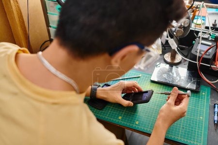 Rückansicht des Reparateurs mit Schraubenzieher, der Diagnose des Smartphones in der privaten Werkstatt macht