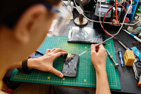 Rückansicht des Technikers, der defekten Touchscreen des Mobiltelefons in der Reparaturwerkstatt abschaltet