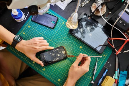 Ausgeschnittene Ansicht des Technikers, der kaputten Touchscreen des Smartphones in der Werkstatt abschaltet