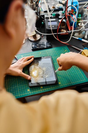 back view of skilled repairman removing broken screen of digital tablet working in private workshop