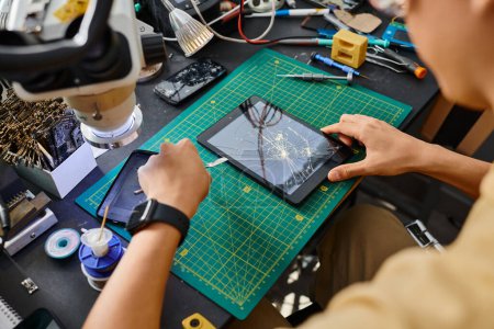 abgeschnittene Ansicht eines professionellen Technikers, der den kaputten Bildschirm des digitalen Tablets in der Werkstatt abschaltet