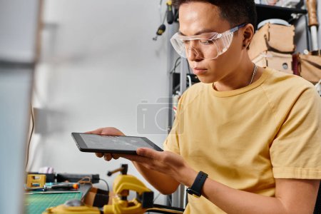 Foto de Atento asiático reparador en gafas celebración digital tablet con roto pantalla táctil en taller - Imagen libre de derechos
