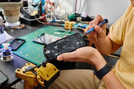 Ausgeschnittene Ansicht des Technikers, der den kaputten Touchscreen des Mobiltelefons mit einem Schraubenzieher abschaltet