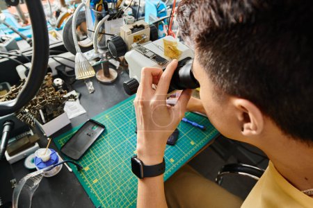 high angle view of skilled repairman working with microscope and electronic equipment in workshop