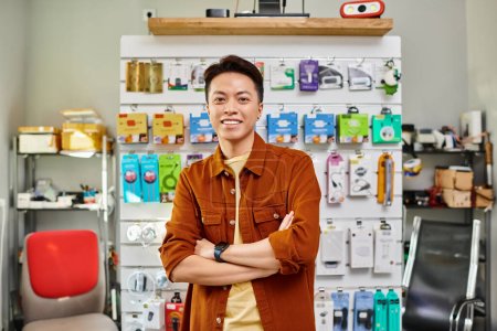 happy asian store manager smiling at camera near counter of private electronics shop, small business